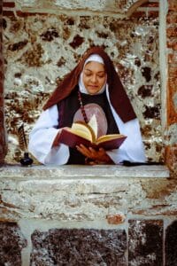 senior nun in stone window frame reading a book